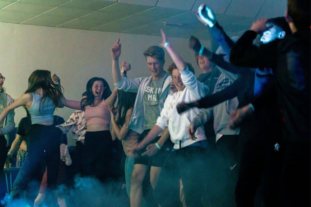 A group of teenagers jumping and dancing with their arms in the air at a RELENTLESS event.