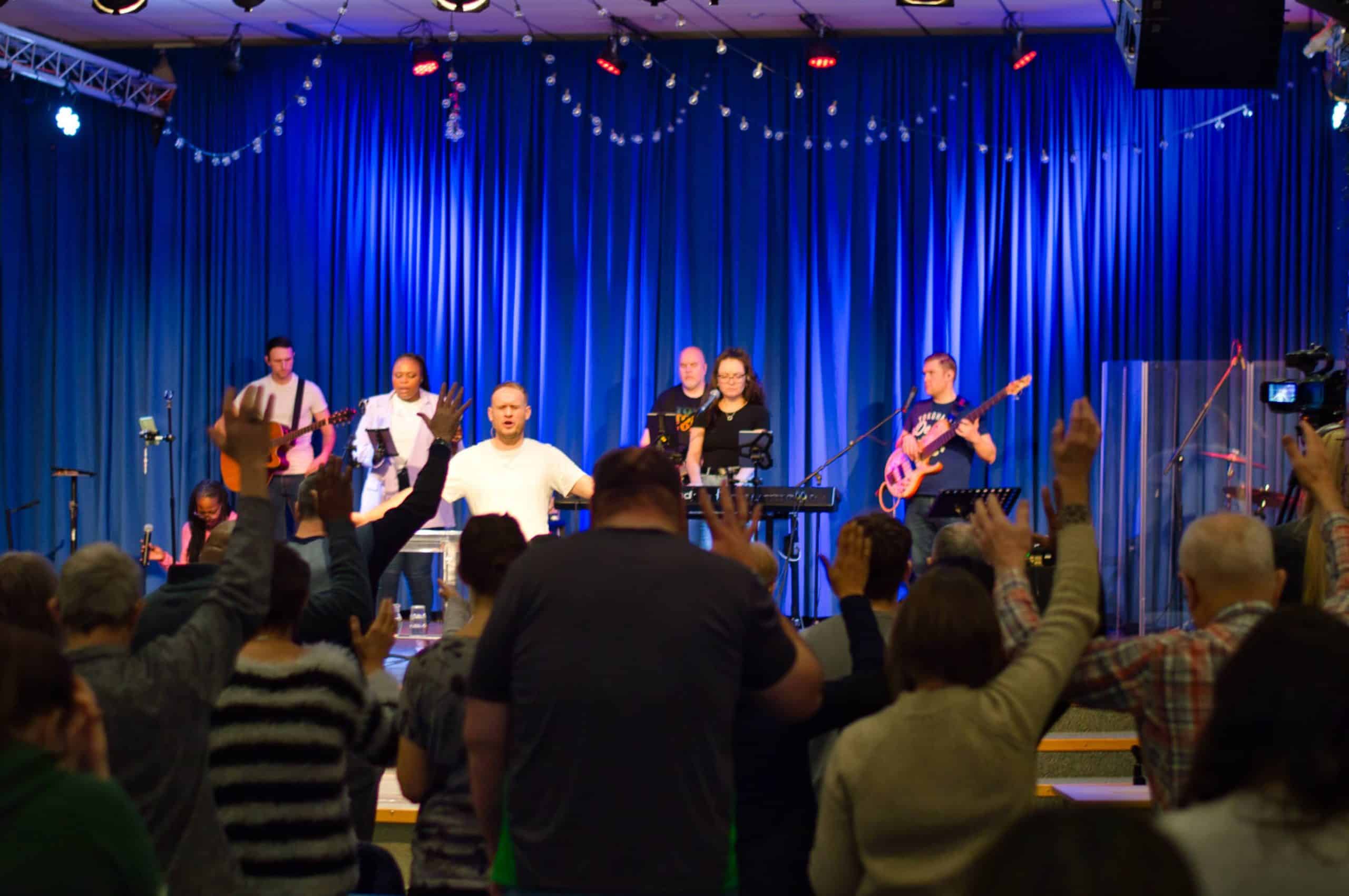 The worship team on stage leading worship at TVCC, the congregation stood with their hands raised in worship
