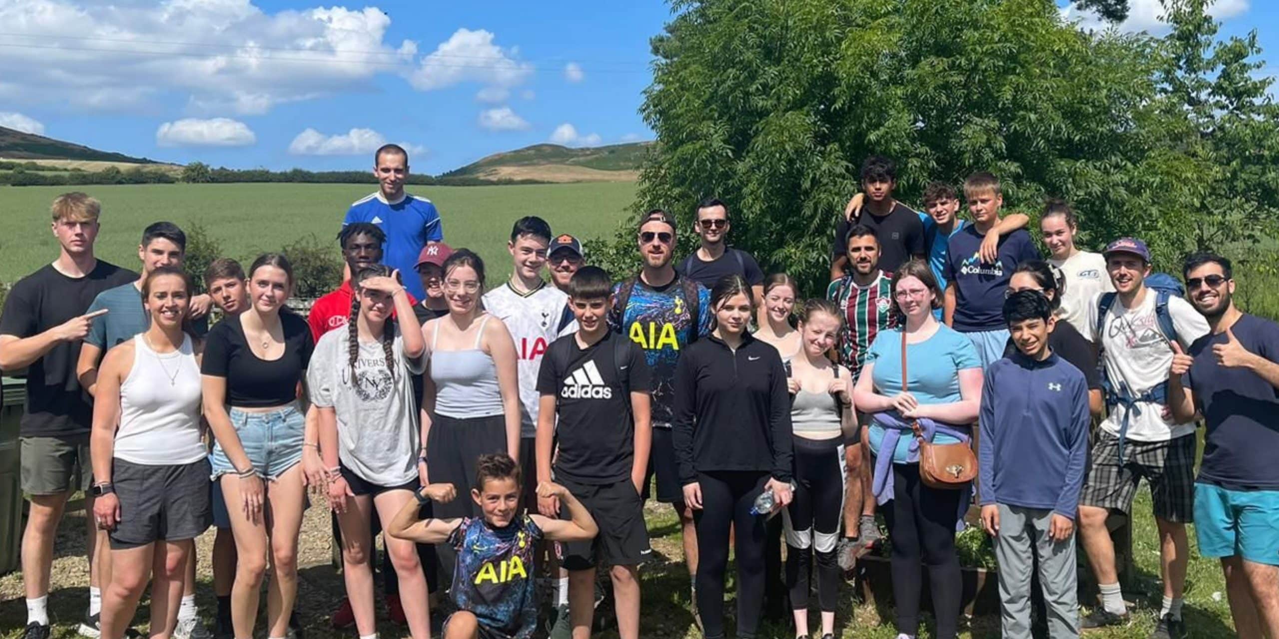 A large group of TVCC youth and leaders posing for a group photo on a walk in the countryside. It is a hot summer day