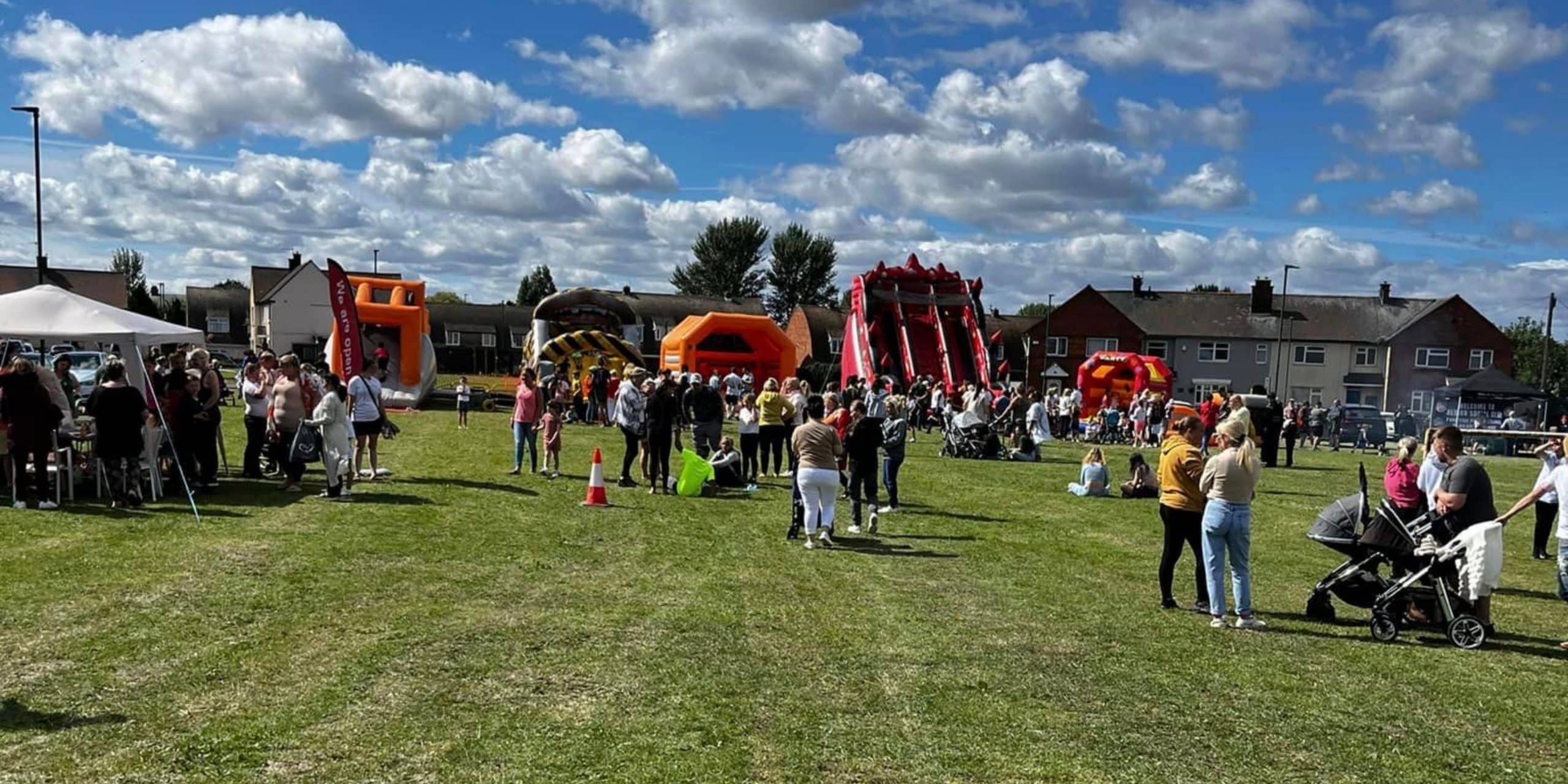 A bright and sunny day on a grass field with large inflatables, gazebos and a large crowd